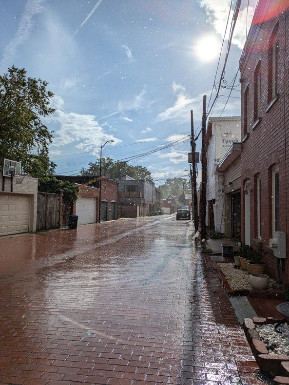 Sun shines through rain in an alley paved with bricks