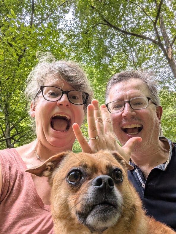 selfie of happy woman with engagement ring, happy man, and dog 